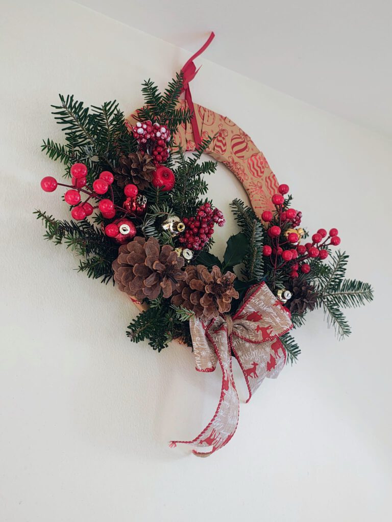 Świąteczny stroik wykonany z szyszek, gałązek igliwia i kokardy.