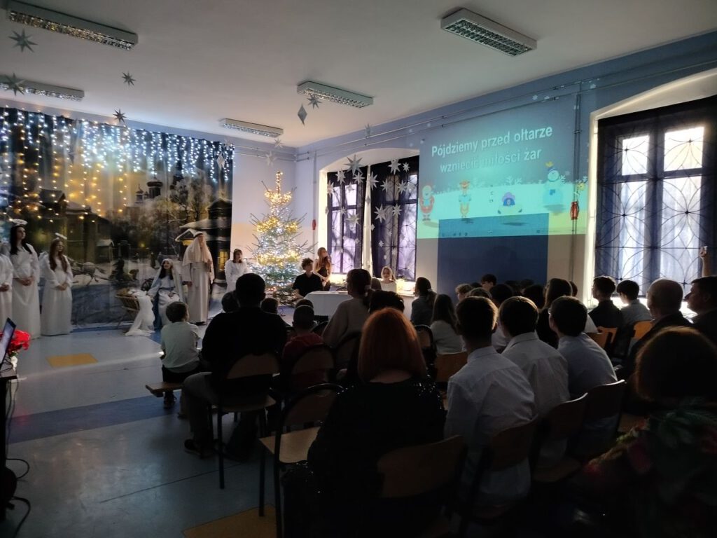 Odświętnie ubrani uczniowie siedzą i śpiewają kolędy.