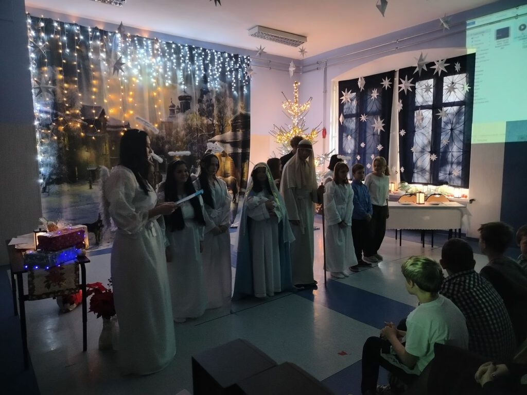 W szeregu stoją uczniowie przebrani za aniołów i śpiewają kolędy.