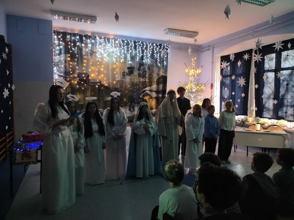 W szeregu stoją uczniowie przebrani za aniołów i śpiewają kolędy.